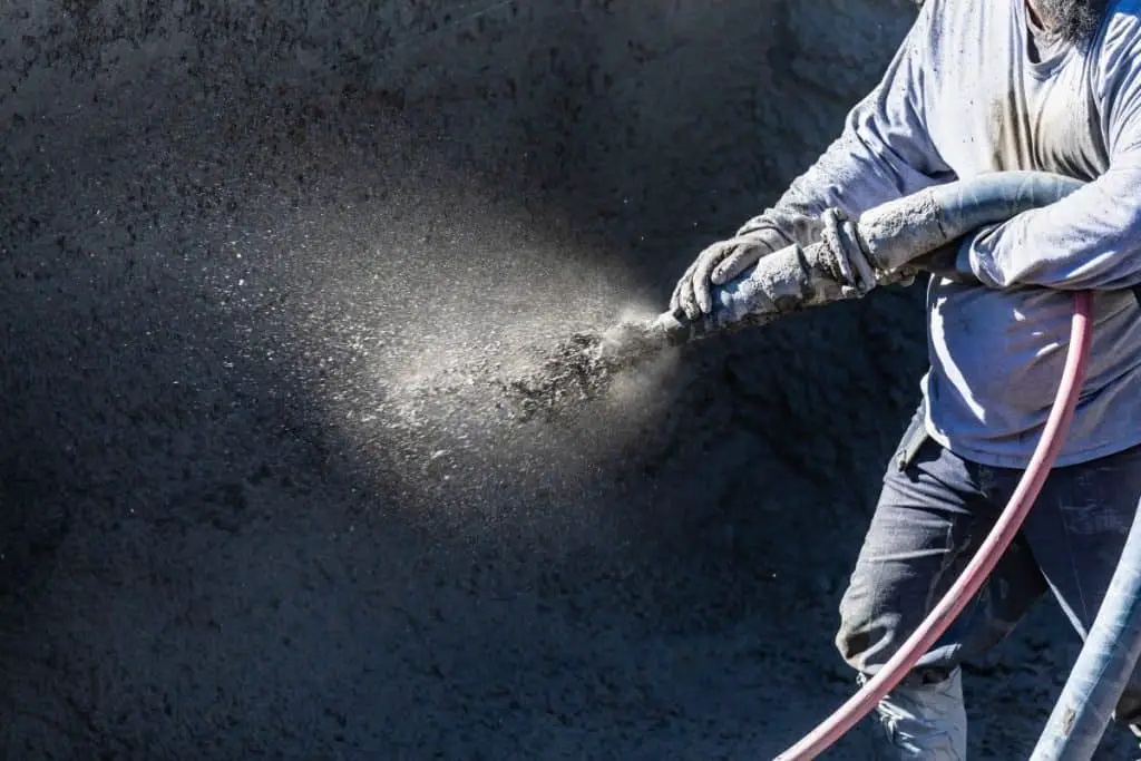 Worker sprays gunite to make a concrete pool.